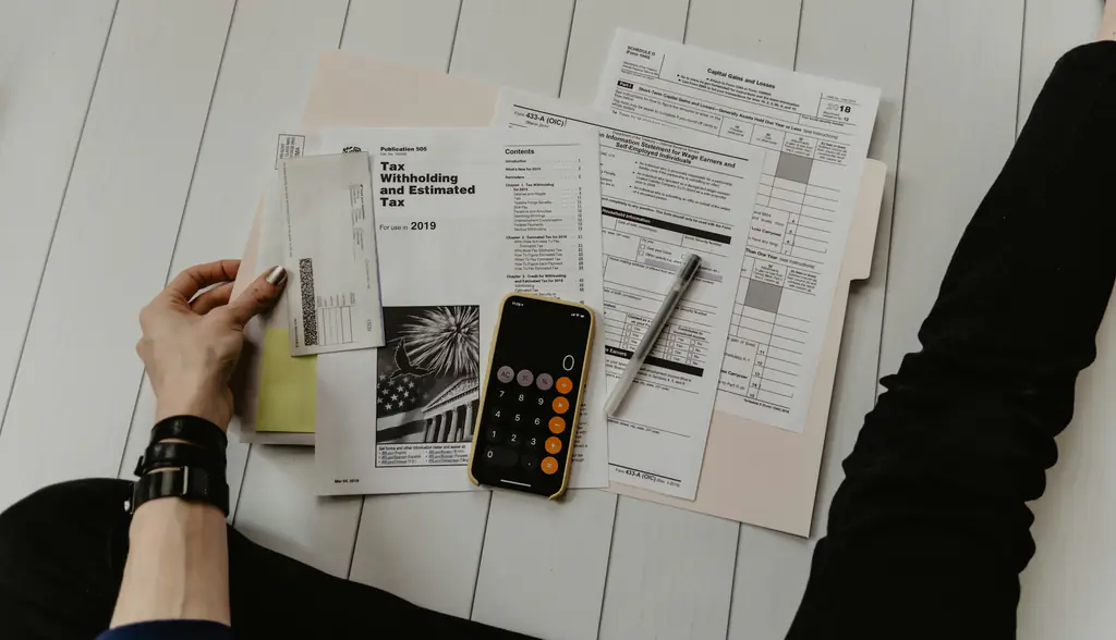 Printed forms, a calculator and a pen spread across a white desk