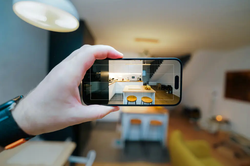A hand holds up a phone, framing a kitchen through the camera viewfinder