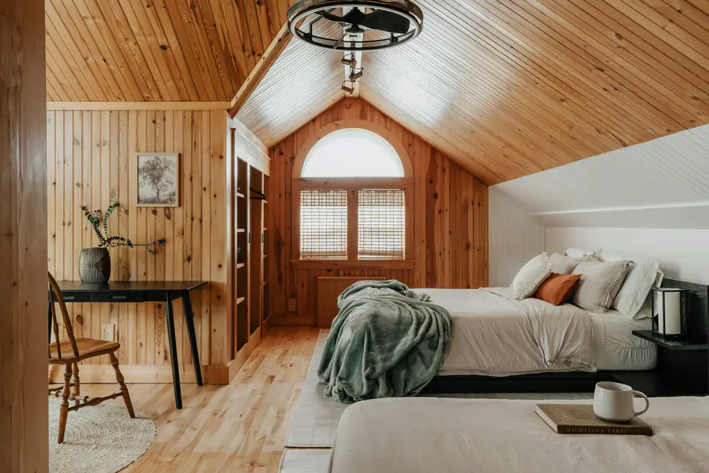 A timber-lined bedroom with two single beds and a desk under the window
